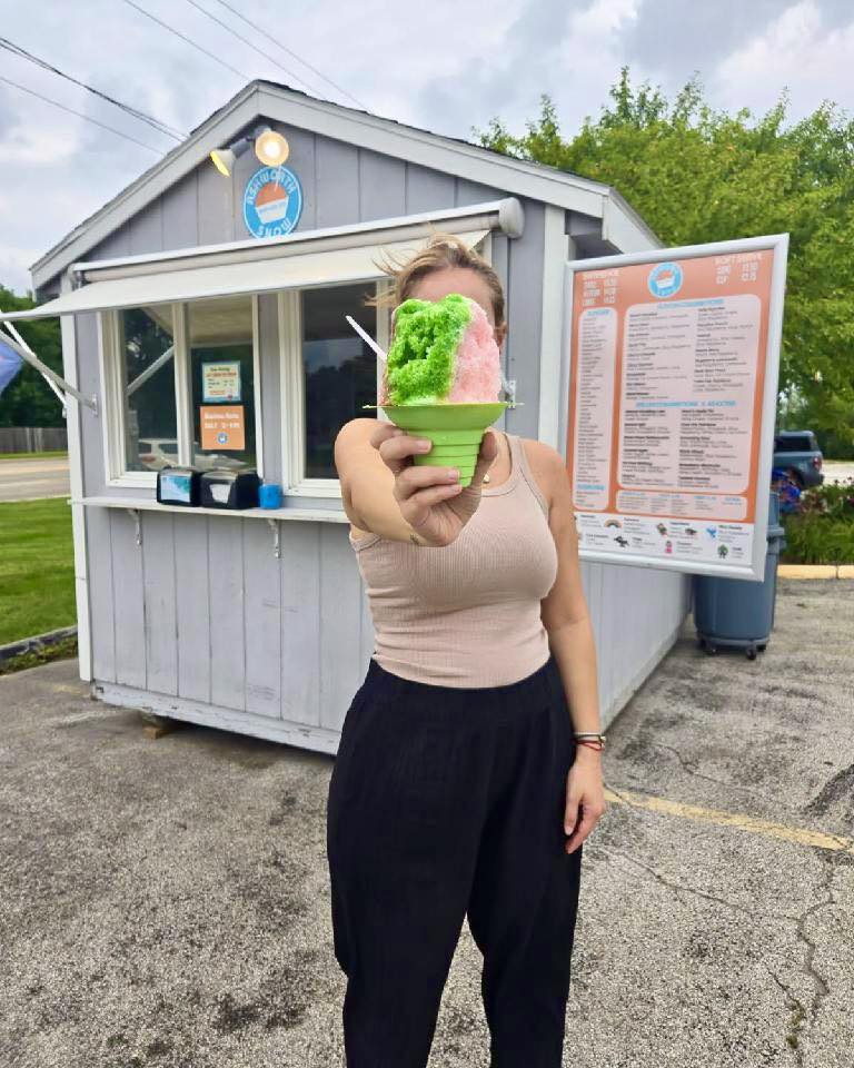 Customer holding a colorful shaved ice in front of the Ashworth Snow stand